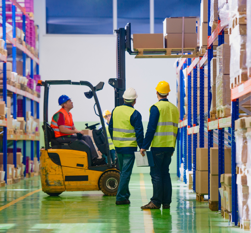 Two warehouse workers watching man in carrier lift pallets