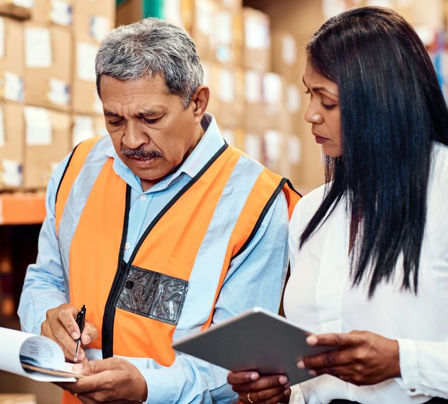 Male and female warehouse workers reviewing clip board and tablet