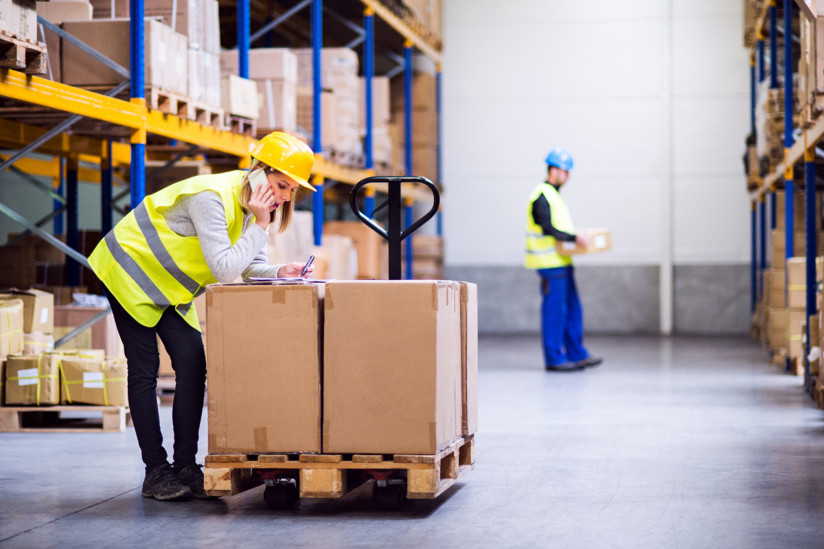 Woman worker in warehouse on the phone and writing on a clipboard